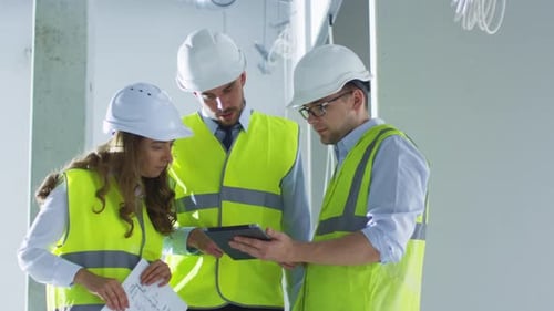 Team of Engineers in Hard Hats Having Conversation, Looking Tablet Computer, inside Building Under
