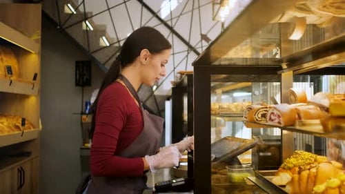 Female baker working in a bakery using the cash register.