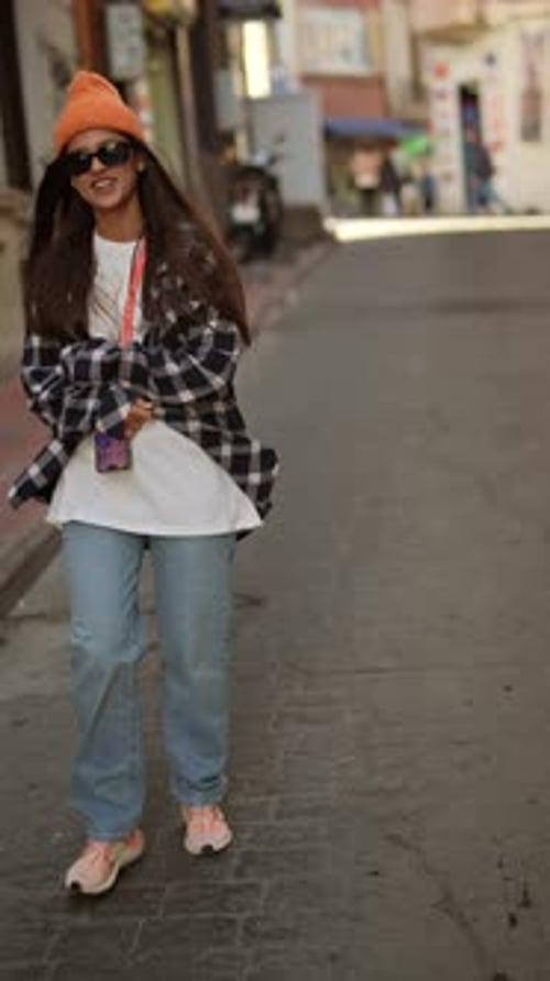 A Fashionable Young Woman Donning Urban Attire and Stylish Sunglasses Confidently Walks in the City
