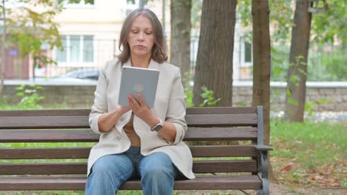 Old Senior Woman Using Digital Tablet while Sitting in Park