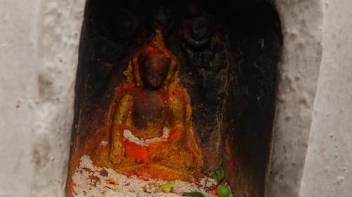 Tilting clip moving to close up of a shrine containing golden statue of Buddha surrounded by flower