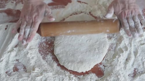 A baker rolls out dough with a wooden rolling pin and begins to prepare bread and pizza.