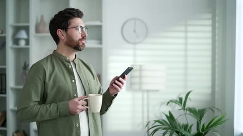 Man Uses Phone and Drinks Coffee at Home