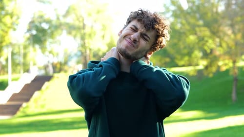 Young Man Stretching Neck in Bright Sunny Park