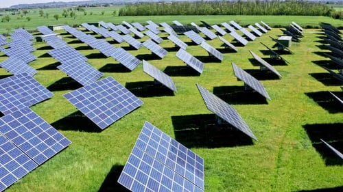 Rows of solar panels on a green field under a clear sky, aerial view