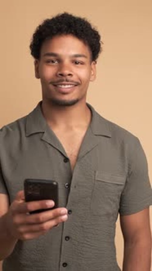 Smiling Young Man Using Smartphone in Beige Studio