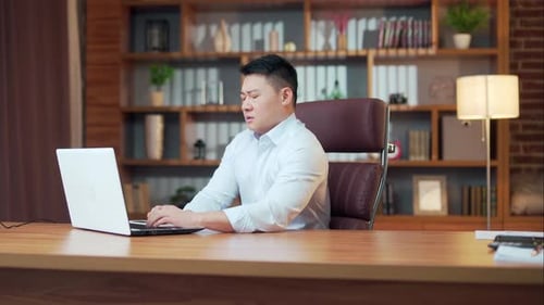 Exhausted, overworked asian office worker sitting in the office with a headache massaging head.