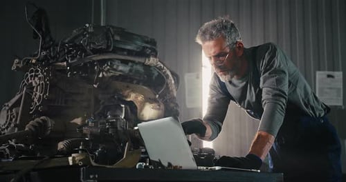 Two Mechanic Caucasian Man in Large Garage Inspecting Parts Under Raised Car