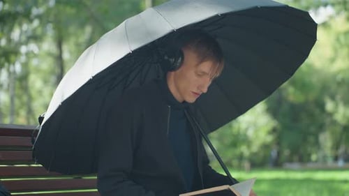 Man reading under umbrella sitting on park bench