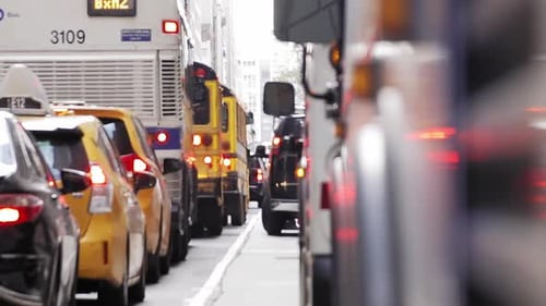 Trânsito diurno da cidade de Nova York com ônibus, carros, táxis e pedestres carregando algo na van.
