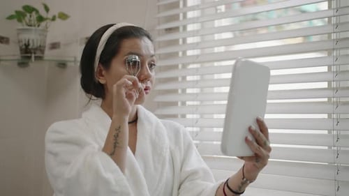 Woman Curling Eyelashes in Bathroom