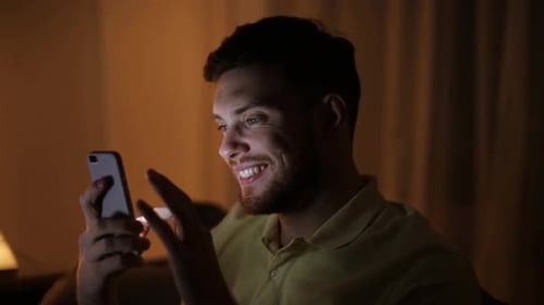 Smiling Man Using Smartphone at Night Indoors