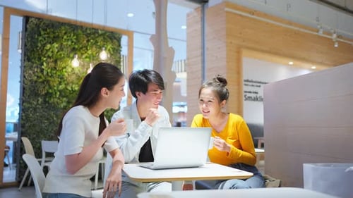 Group of Asian friends talking and using laptop computer in restaurant.