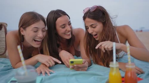 Zwei Freundinnen teilen sich ein Mobilgerät, um am Strand soziale Medien zu überprüfen Frauen checken das Smartphone