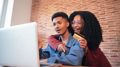 A Cheerful African American Couple is Using a Laptop to Search a Sale on a Online Shop Excited