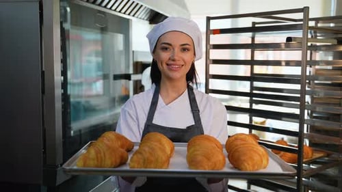 Smiling Baker Holds Tray of Fresh Croissants