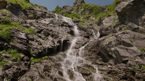 Large waterfall rushing through rocks down a mountain on a sunny day.