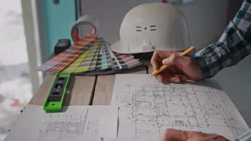 A Man Sitting at a Table Drawing a Blueprint with a Pencil