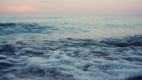 Blue sea waves splashing sand seashore at cold morning sunrise twilight