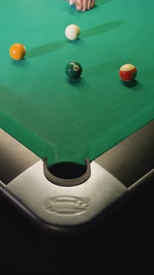 Up Shot of Hand Using Cue Stick to Strike White Billiard Ball on Green Pool Table