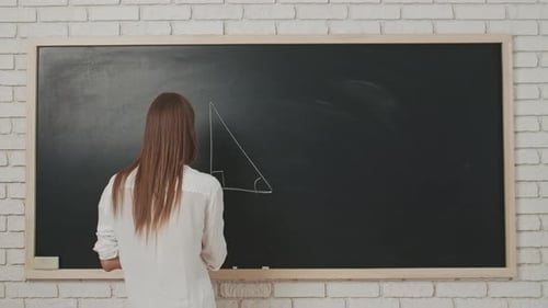 Young Woman College Teacher in Classroom Stands in Front of Chalkboard Explains Geometry Lesson to