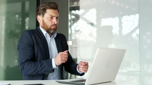Businessman in a formal suit froze while working on laptop sitting at workplace in business office.