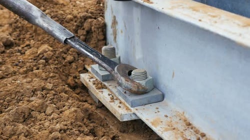 Worker Twists Screw on Metal Tower Support on Ground