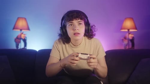 Attractive curly-haired young gamer girl sitting on couch and playing an online video game