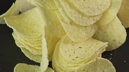 Close up potato chips rotate on black background. Snack for drinks. Golden fried potatoes. Crispy