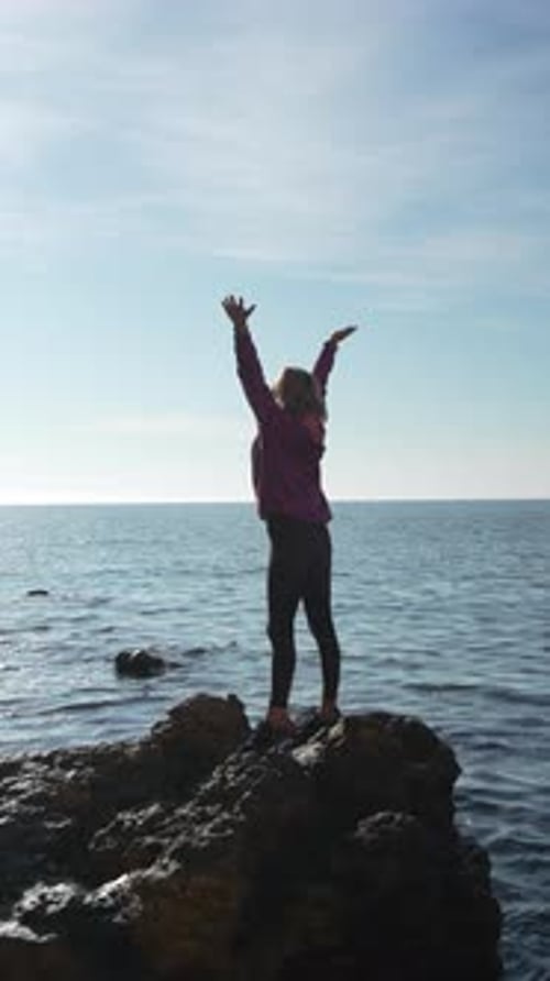 Woman Ocean Victory Silhouette Celebrating Freedom on a Rocky Shore During a Bright Sunny Morning