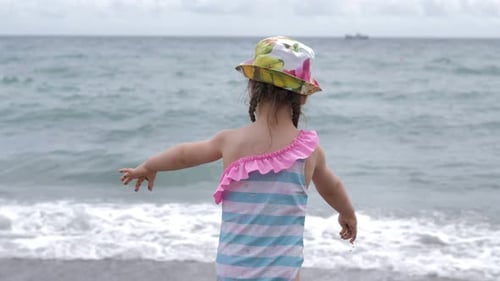 Cute 3 Years Old Girl in a Swimsuit and Armbands is Playing with Pebbles on Black Sea Beach