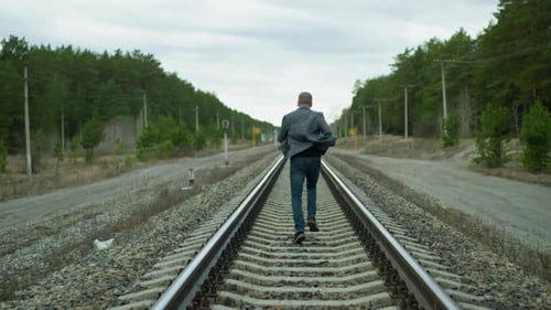 Man Walks on Railroad Track Through Forest