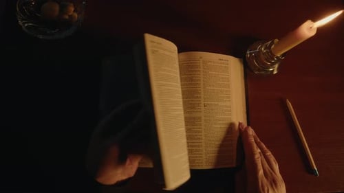 Hands Turn Pages of Book by Candlelight