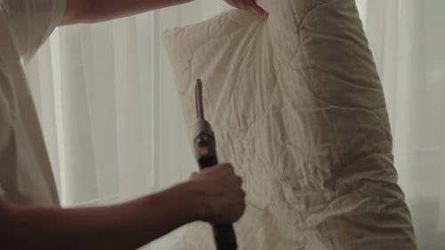 Housekeeper Using Steam Cleaner on White Blanket in Hotel Room Promoting Hygiene and Freshness for