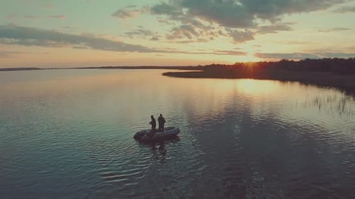 Friends fishing at sunset. Two amateur anglers fishing from the boat on a clam lake during sunset