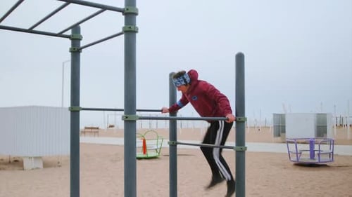 Male Athlete Performs Swing At Seaside Park Caucasian Male Excercises On Playground Equipment Near