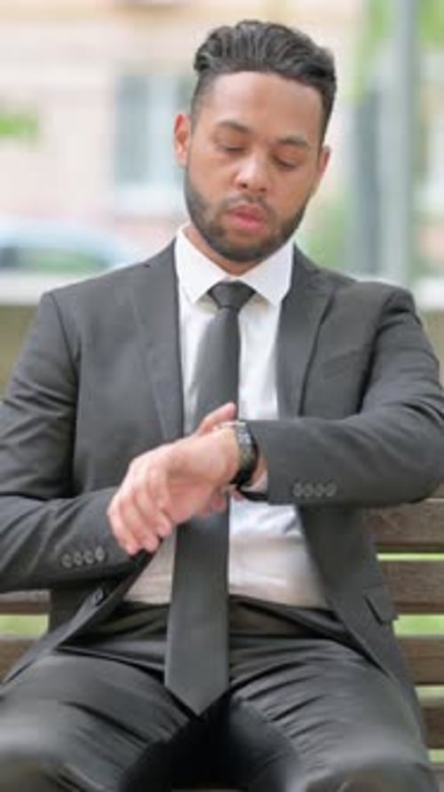 Man in Suit Sits on Bench Checking Watch