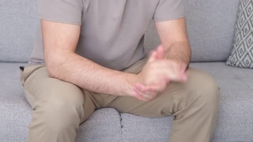 Man Rubs His Hands Together Indoors on Couch