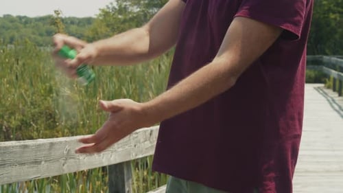 Man Spraying Insect Repellent By the Lake on a Bright Sunny Day