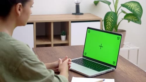 Una estudiante mira la lección en línea en una computadora portátil con pantalla Chromakey mientras está en casa