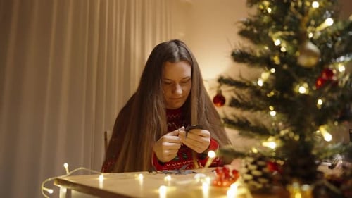 Woman Crafts Holiday Decorations by Christmas Tree