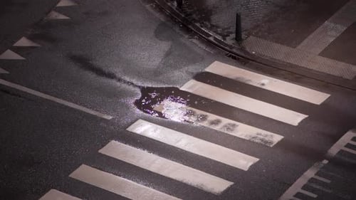 Toma de ángulo alto de gotas de lluvia en un charco en el paso de peatones de la calle de la ciudad por la noche