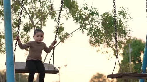 slow motion of cheerful child girl playing on a swing at playground