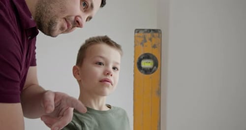Le fils utilise un niveau pour garantir la précision, faisant preuve de patience et de compétences