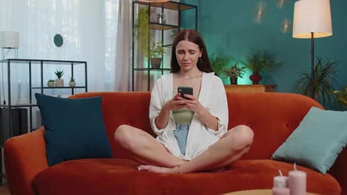 Upset Woman Looks at Phone on Couch