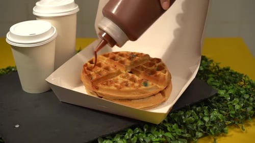 Hinzufügen von süßen Süßigkeiten mit Milchkaramell als Topping in Zeitlupe zu Waffeln
