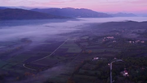 Aerial view of foggy valley and mist-covered mountains in sunrise, Italy.