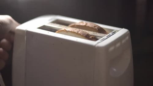 Person Making A Toasted Bread Using A White Toaster For Breakfast In The Kitchen. -close up shot