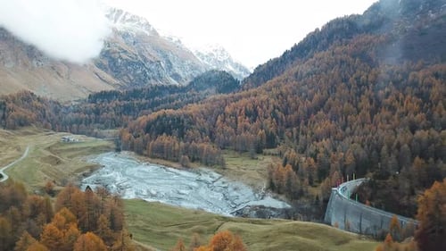 Vista aérea de uma estrada sinuosa através de um vale cercado por densas florestas cor de outono, com monte
