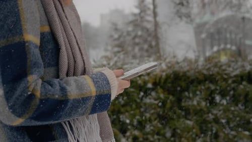 Woman enjoys a snowy walk in the park while using her smartphone